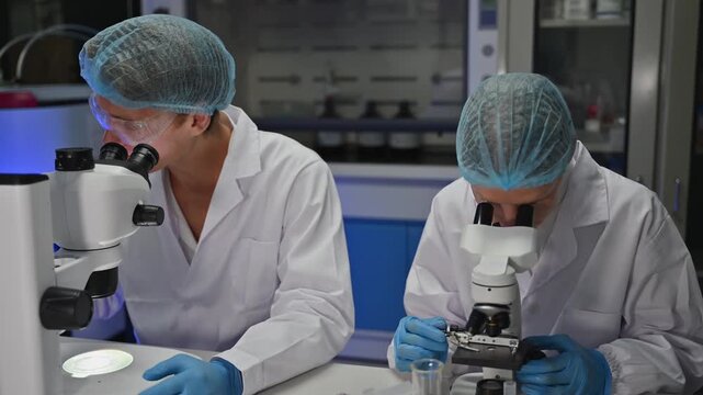 Male And Female Biology Colleague Use Microscope For Examine Virus Sample Inside Laboratory