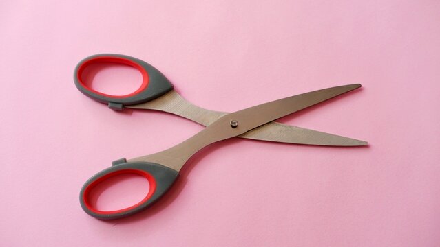 
Open sharp steel scissors with grey and red handles isolated on a pink background. Top view of stationery tool for cutting paper, crafts, and office work. Professional cutting equipmen