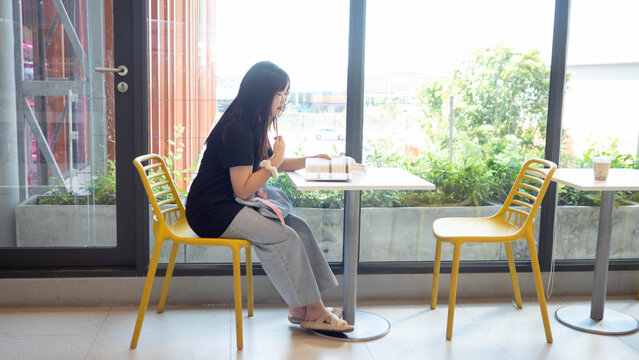 A young Asian female student writing on a notebook and learning in a library or coffee shop. Concept of exam preparation, academic success, and youth lifestyle isolated on a blurry background.
