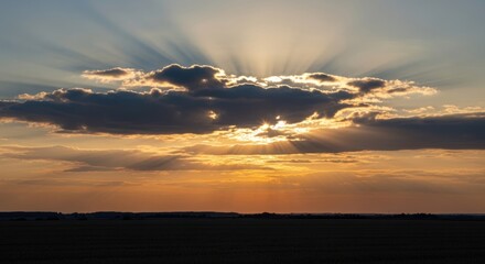 Fototapeta premium Golden sunset with bright sun rays breaking through dark clouds over flat horizon, for hope divine inspiration while for new beginning spiritual peace mind