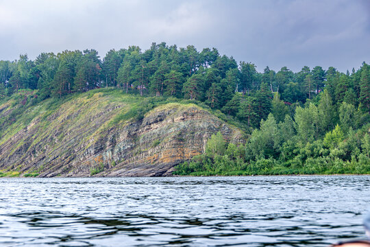 Tilted sedimentary strata forming a monocline structure along a riverbank with dense forest vegetation