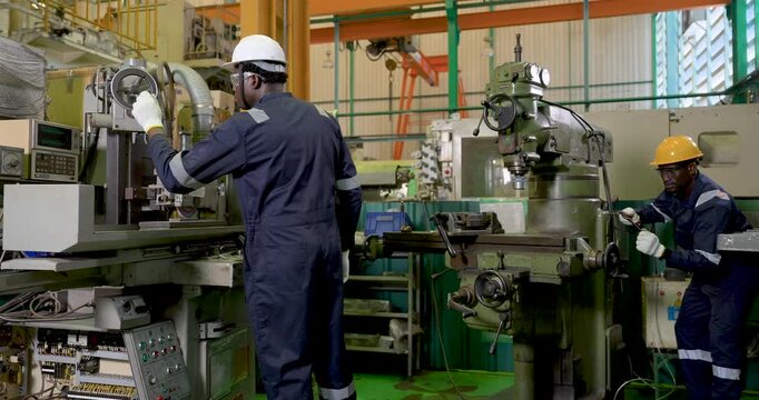 two african adult male workers manage parallel machining stations in workshop, one checks control unit while one adjusts machine, safety PPE teamwork supports production flow