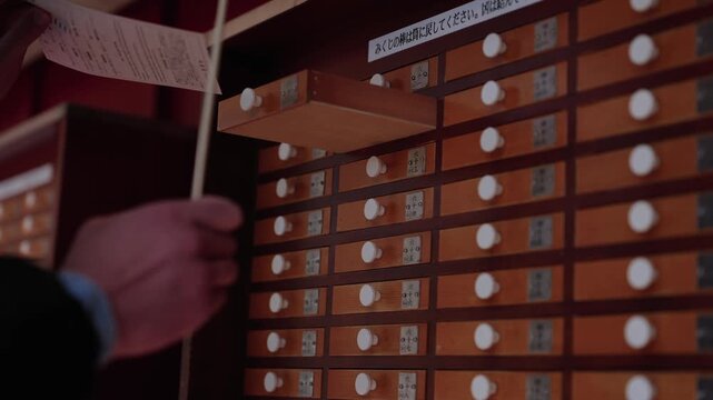 Hands pulling fortune stick from numbered wooden omikuji drawer cabinet at Japanese shrine Japan