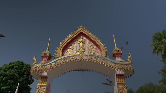 Camera tilting down from the sky with a palm tree and temple gates as it pushes into Don Khon Buddhist temple in Laos.