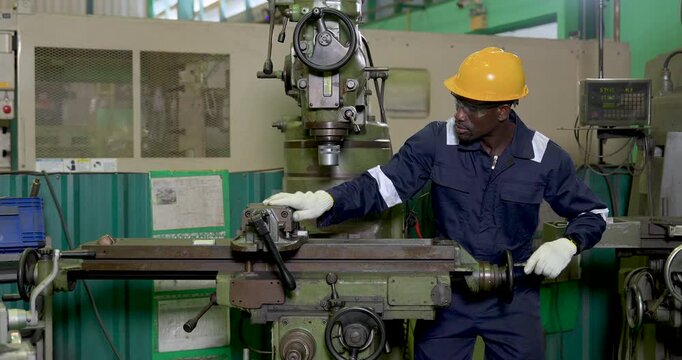 African adult male operator stands at industrial milling machine, turning handwheel and checking table position for production adjustment, quality control and safe manufacturing workflow in workshop