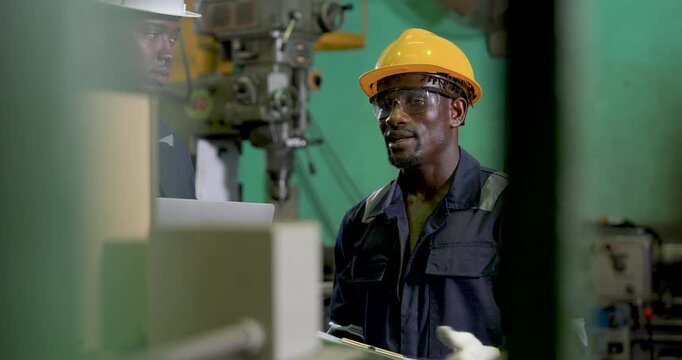 african adult male engineer stands alert near machine zone after team review, monitoring workshop activity in , safety compliance and production workflow supervision continue