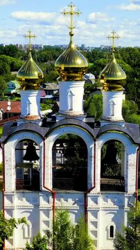 Vertical video. Pereslavl-Zalessky, Russia. St. Nicholas Pereslavsky Monastery, white cathedral with golden onion domes and triple-arched bell tower, aerial pullback under summer clouds. Drone footag