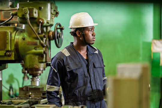 African male technician pauses near industrial drill, reviews machine position and shop floor activity in manufacturing plant, supports smart factory supervision, safety control, production readiness.