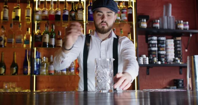 Barman working. Cocktail preparing. Professional bearded male bartender scooping ice cubes into transparent glass mixing rocks using bar spoon.