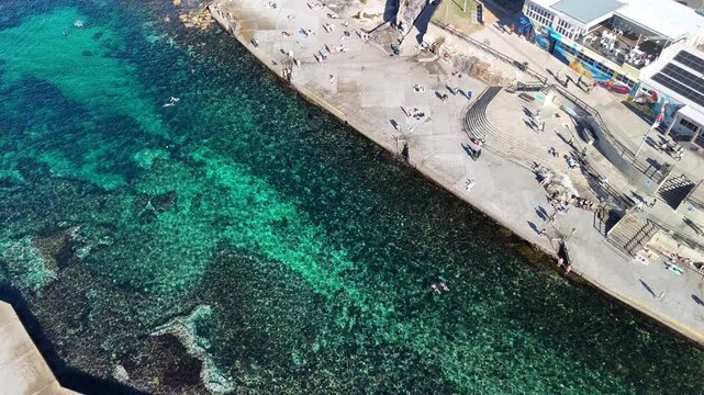 Aerial Roll of Clovelly Bay Australia on a crystal clear ocean sunny day with some people sunbathing and swimming 