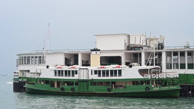 A historic green and white Star Ferry remains docked at its Victoria Harbour pier on a misty morning. Highlights the traditional maritime commute and colonial-era transit charm of Hong Kong SAR.