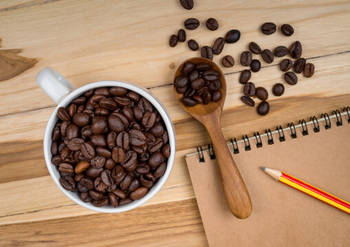 Roasted Coffee Beans in White Cup with Wooden Spoon and Notebook on Table