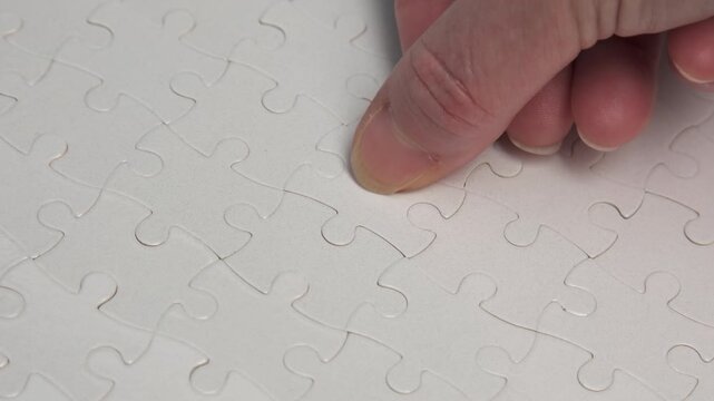 Human hand completing white jigsaw puzzle putting last final piece close-up, successful solution of problem
