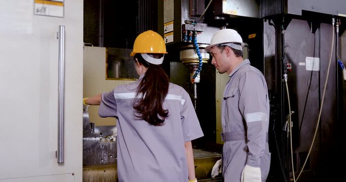 Asian woman technician and Asian man engineer inspect CNC machine interior, review metal surface, and coordinate production line check inside smart manufacturing plant with PPE and safety protocol