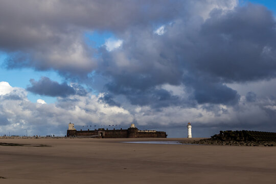 Fort Perch Rock and Perch Rock Lighthouse seen across New Brighton beach with dramatic clouds and patches of blue sky above