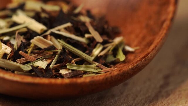  Loose leaf herbal tea blend with dried citrus peel and lemongrass stems on wooden spoon, close-up, macro.