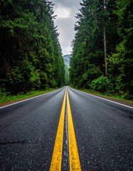 Obraz premium An asphalt highway curves through a green summer forest and winding mountain landscape under a bright sky, offering a scenic rural travel way for a nature drive or country trip