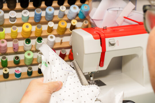 Person's hand cutting polka dot fabric pattern with scissors, preparing for crafts with a sewing machine and thread spools