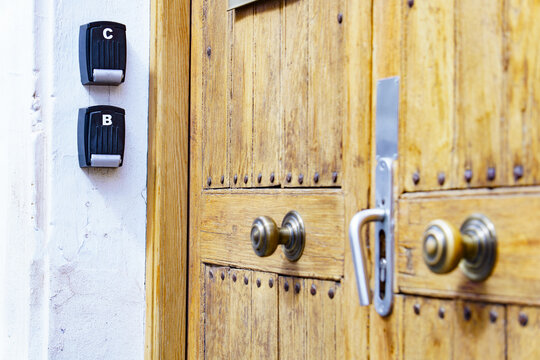 Key lock boxes b and c mounted on a wall next to an aged wooden door with antique brass doorknobs and a modern handle