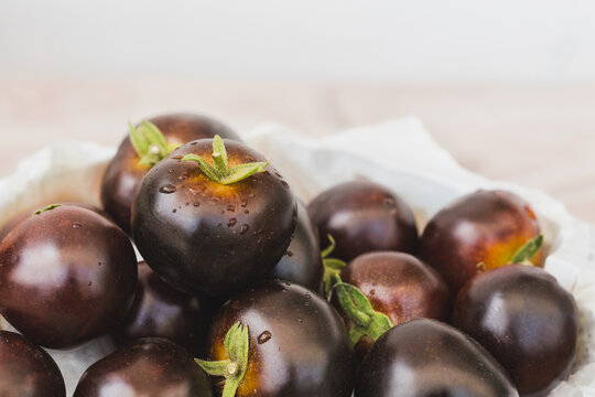 Fresh harvest of dark purple Indigo Rose heirloom tomatoes with water droplets in a bowl.