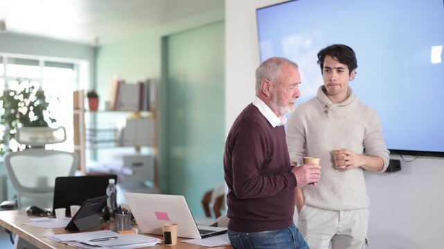 Coffee break at office. Two men chat and laugh during break, informal communication of colleagues, friendly conversation.