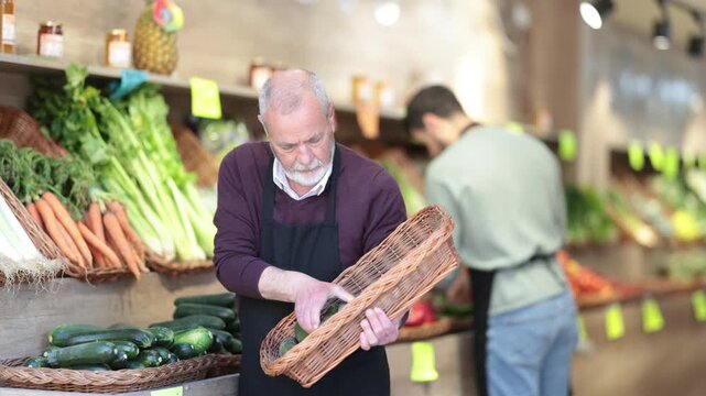 Mature seller working in supermarket and lays out fresh zucchini on counter. High quality 4k footage