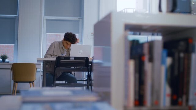 Young tired man feeling overwhelmed with homework while studying for an exam in a public library
