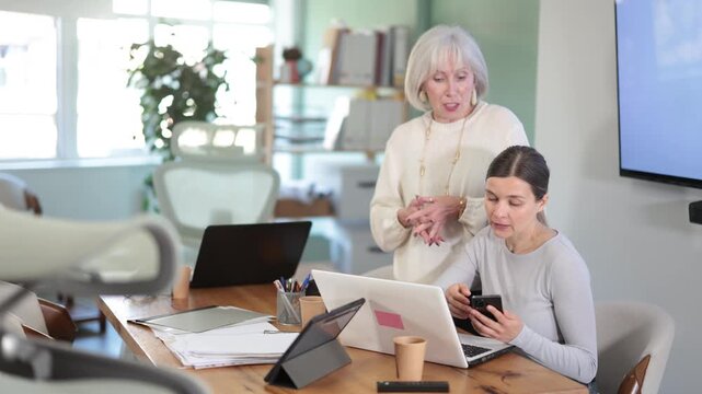 Senior woman boss found female subordinate idling and scrolling phone, mentor shouts at subordinate. Scrolling of phone and social networks, procrastination at work, evading official duties.