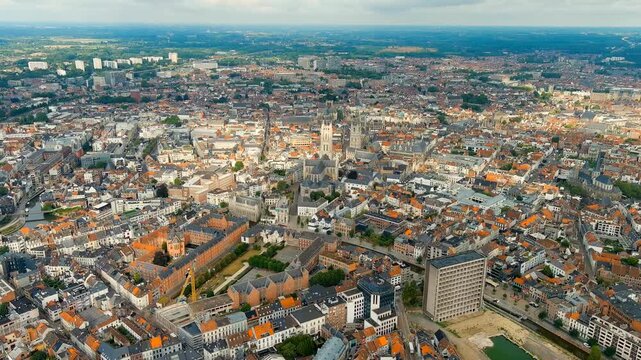 Ghent, Belgium. Saint Bavo's Cathedral, its 89-metre Gothic tower rising above a dense weave of terracotta rooftops, aerial panoramic view over the historic Flemish city under soft summer cloud cover