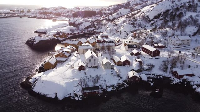 Sunny day drone shot of Nusfjord village in Lofoten Islands, snowy peaks surrounding the quiet ocean harbor. Bright winter atmosphere in a preserved Norwegian fishing settlement