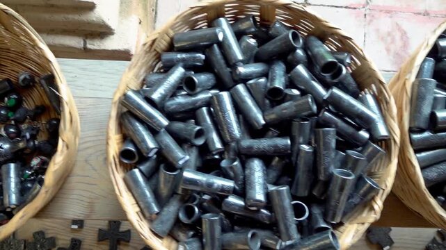 Closeup view of handcrafted metal parts decorative components and cylindrical fittings stored inside woven baskets in artisan workshop environment.