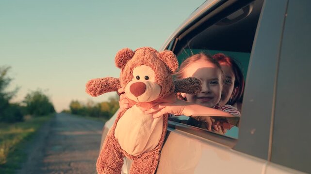 little girl with toy bear. happy face child daughter from window with teddy bear. happy family. mother daughter traveling car. happy mother child back seat car going trip. face childish smile.
