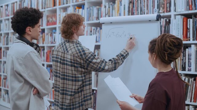 Group of young university students collaborating on a difficult math equation in a library