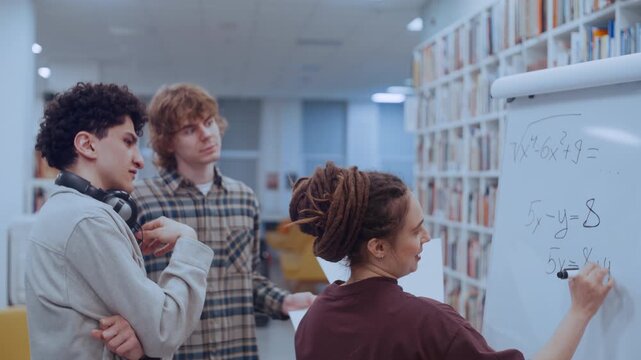 Two curly-haired male students and their dreadlocked female partner work together to solve a challenging algebraic problem. 
