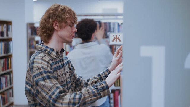 Two young male students searching for specific books on bookshelves in a modern library