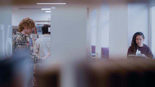 Book selection happens at the shelves as a pair of learners discuss which texts to borrow. Behind them, a girl with dreadlocks sits with her back to the window, completely immersed in a novel