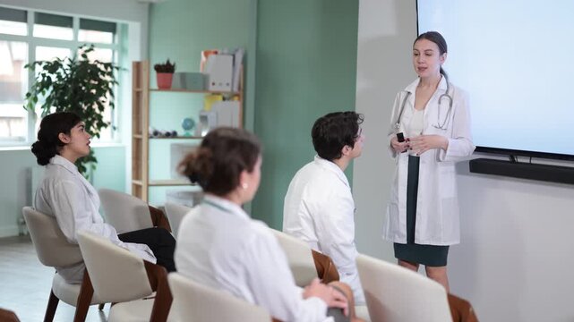 Young female doctor in medical gown with remote control gives presentation to colleagues doctors in conference room