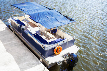 Pontoon boat with blue canopy moored near a concrete pier on a sunny day ©  Tsvyk L.