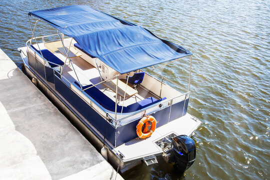 Pontoon boat with blue canopy moored near a concrete pier on a sunny day