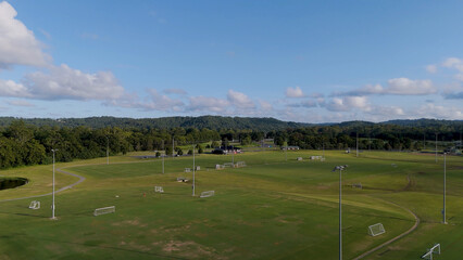 Obraz premium Wide Aerial View of Green Soccer Fields and Forested Hills Under Blue Sky