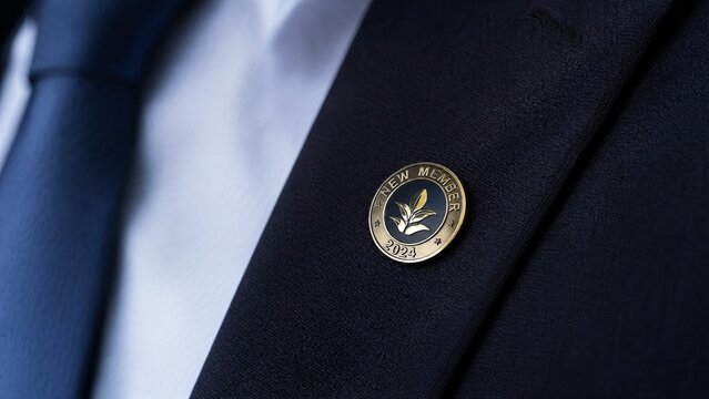 affiliation. New membership pin on dark suit lapel, polished metal, elegant composition. pitch deck slides, case study pages, designed for enterprise HRIS and productivity software interfaces.