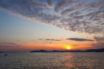 Fototapeta premium Golden sunset coloring the sky and sea over the tranquil Gulluk bay in Turkey, with distant mountains and a small boat