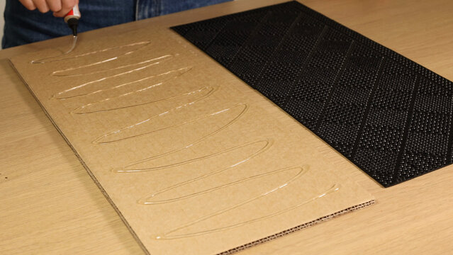 Person Applying Liquid Adhesive in Zigzag Pattern to Cardboard Sheet