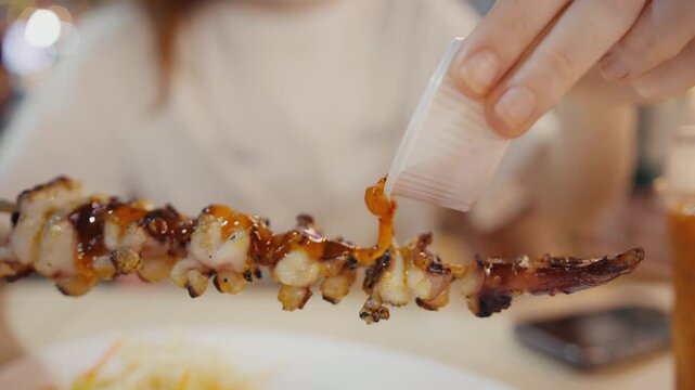 Pouring spicy sauce on grilled squid tentacle skewers