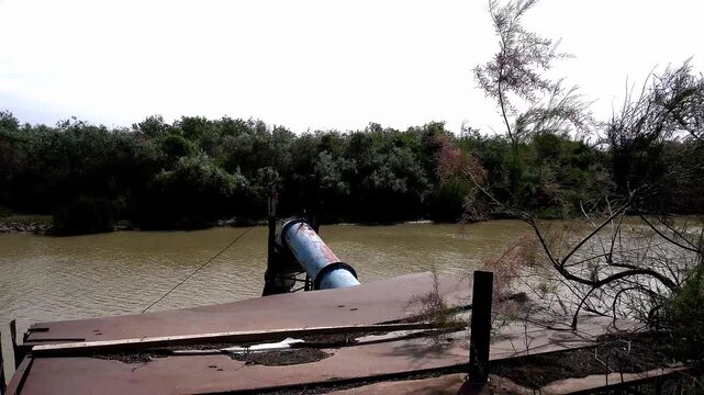 4K shot of a large rusty water pump pipe with a canal and Tugai forest in the background