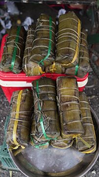 Traditional Vietnamese Banh Tet rice cakes wrapped in banana leaves for sale. Close-up of stacked Lunar New Year holiday food at a street market counter in Nha Trang, Khanh Hoa province, Vietnam.