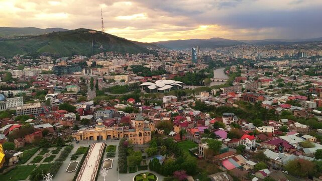 Aerial cityscape of Tbilisi, Georgia at sunset, drone revealing golden dome and upper architecture of the Holy Trinity Cathedral (Sameba)