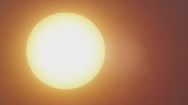 Extreme close-up of an intense glowing sun orb and radiant heat waves in a hazy orange sunset sky, excellent for climate change and summer concepts.