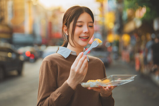 Happy young Asian woman enjoying eating famous Thai mango sticky rice dessert at Yaowarat Chinatown street food market in Bangkok, Thailand. Culinary tourism, travel lifestyle, Authentic local food