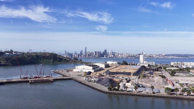 Morning drone view flying over Treasure Island in San Francisco bay, showing ongoing construction projects with the iconic downtown city skyline and Yerba Buena island in the background